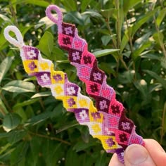 someone is holding up a small piece of beaded fabric in front of some bushes