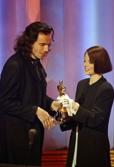 a man and woman standing next to each other in front of a microphone holding an award