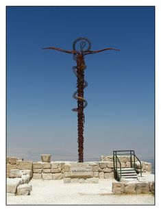 a large metal cross on top of a stone wall next to a stair case in the desert