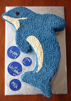 a birthday cake shaped like a dolphin on top of a sheet of paper with buttons