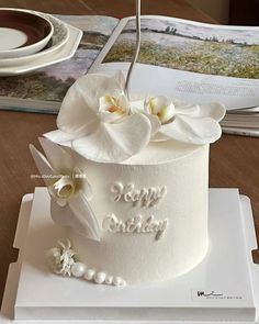 a white cake decorated with flowers and pearls on a table next to an open book