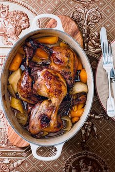 a pot full of chicken and vegetables on top of a table with silverware next to it