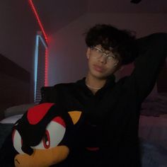 a young man holding a stuffed animal in his arms and posing for the camera with red light behind him