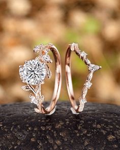 two wedding rings with leaves and diamonds on top of a rock in front of some rocks