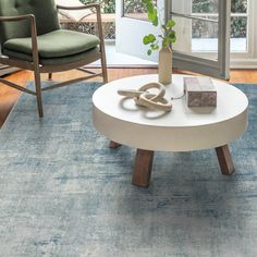 a living room with a blue rug, chair and coffee table in front of a window