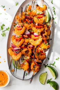 grilled shrimp skewers on a plate with lime wedges and dipping sauce