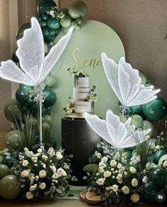 a table topped with lots of white flowers next to green balloons and cake on top of it