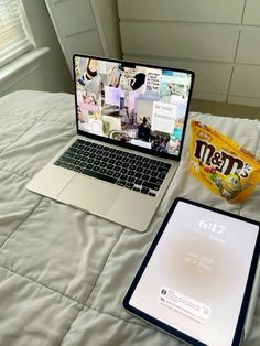 an open laptop computer sitting on top of a bed next to a book and tablet