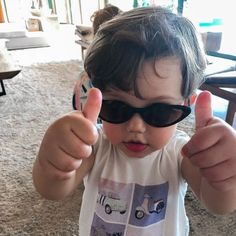 a little boy wearing sunglasses giving the thumbs up sign with his thumb and eyeglasses on