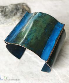 a green and blue cuff bracelet sitting on top of a white table next to a rock