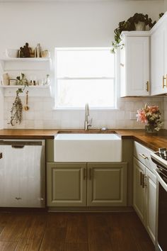 a kitchen with wooden floors and white cabinets, an open window above the dishwasher