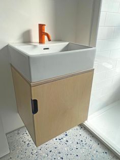 a white sink sitting next to a wooden cabinet in a bathroom under a shower stall