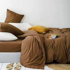 a bed with brown sheets and pillows on top of it next to two pairs of slippers