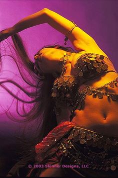 a belly dancer is posing for the camera with her hair blowing in the wind and purple lighting behind her