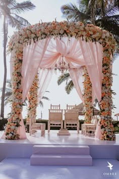 an outdoor wedding setup with pink drapes and white flowers on the altar, surrounded by palm trees