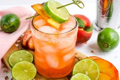 a drink with limes and orange slices on a cutting board next to other fruit