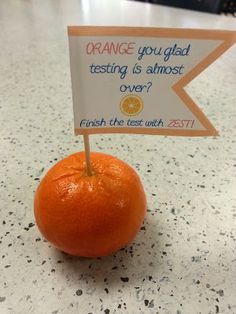 an orange sitting on top of a counter with a sign that says orange you glad testing is almost over