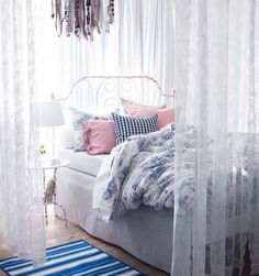 a white bed sitting under a window next to a rug on top of a wooden floor