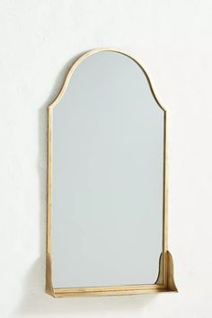 a mirror mounted to the side of a white wall next to a shelf with a gold frame