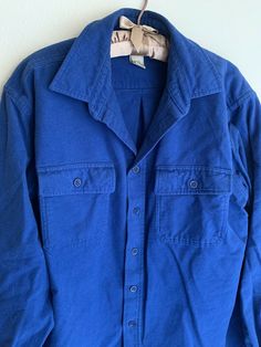 Pre-owned LL Bean shirt. It’s a solid royal blue and feels like a soft brushed cotton/flannel. Tag reads ‘chamois cloth shirt’. Long sleeve & 100% cotton. Buttons down the front & has 2 pockets on the chest. Some overall piling from wear, see up close photo. Has a ‘broken in’ feel but lots of wear left. Would be great to layer or use as a lightweight jacket. Approx. Measurements (laid flat): Tagged size L 20in across shoulders 24in across underarms 29in neck to bottom front (shorter at sides due Blue Long Sleeve Shacket With Pockets, Blue Collared Shacket With Buttoned Pockets, Long Sleeve Cotton Shacket With Buttons, Cotton Long Sleeve Shacket With Buttons, Blue Cotton Shacket With Button Closure, Blue Collared Shacket, Vintage Washed Blue Top With Buttons, Blue Workwear Shacket With Buttoned Pockets, Blue Collared Shacket With Buttons