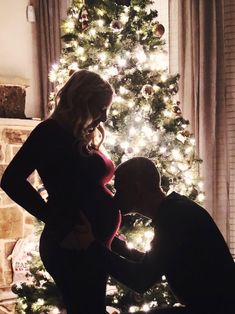 a man and woman standing in front of a christmas tree with their hands on the pregnant belly