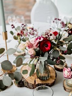 the table is set with flowers and greenery in glass vases on wood slices