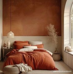 a bed with an orange comforter and pillows in a bedroom next to a window