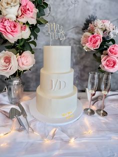 a three tiered white wedding cake with pink flowers and silverware on the table