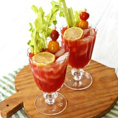 two glasses filled with red liquid and garnish on top of a cutting board