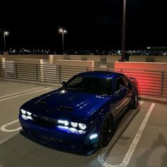 a blue sports car parked on the side of a road at night with its lights on