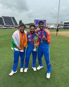 three men standing next to each other on top of a field holding a trophy in their hands