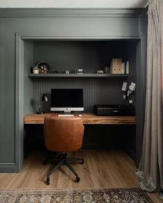 a desk with a computer on top of it in front of a book shelf and window