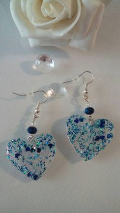 a pair of blue heart shaped earrings next to a white rose on a tablecloth