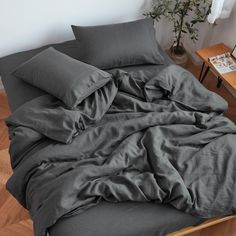 an unmade bed with grey sheets and pillows on it in a room next to a table