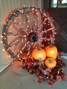 some pumpkins are sitting in front of a wagon wheel with fairy lights on it