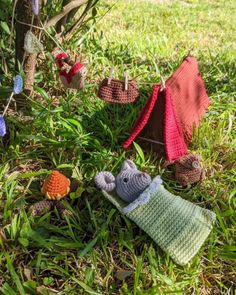 crocheted toys are laying on the grass in front of a tree with clothes hanging from it