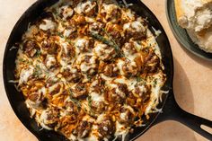 a skillet filled with meatballs and cheese on top of a table next to bread