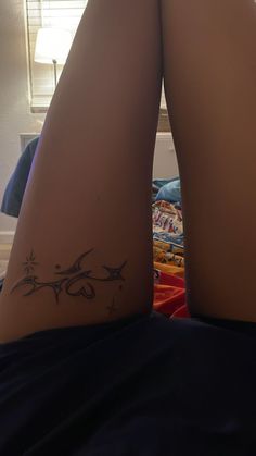 a woman's legs with tattoos on them sitting in front of a bed next to a window