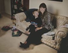 a woman sitting on top of a couch next to a boy in a living room