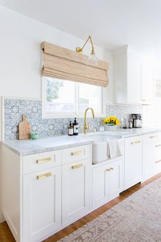 a kitchen with white cabinets and blue tile on the backsplash, gold faucet