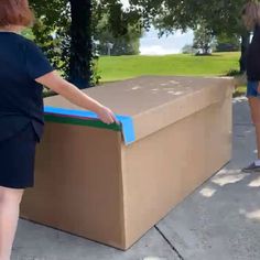 two women standing next to a large cardboard box