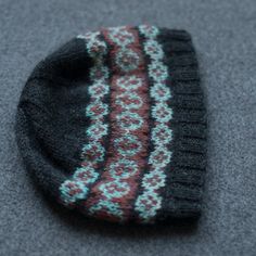 a knitted hat laying on top of a gray carpet covered in grey and red yarn