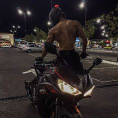 a shirtless man riding on the back of a motorcycle in a parking lot at night