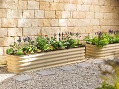 two metal planters filled with plants next to a brick wall and stone flooring