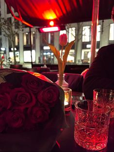 a bouquet of roses sits on a table with two glasses and a vase filled with water