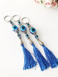 three blue evil eye keychains with tassels on them and flowers in the background