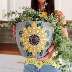 a woman is holding a potted plant with yellow flowers and green leaves on it