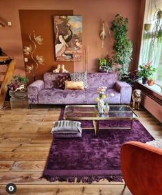 a living room filled with purple furniture and lots of plants on the wall behind it