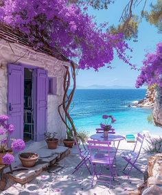 a table and chairs on the beach with purple flowers in front of an open door