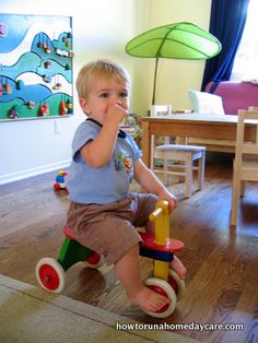 a little boy sitting on top of a wooden toy car in a living room next to a table